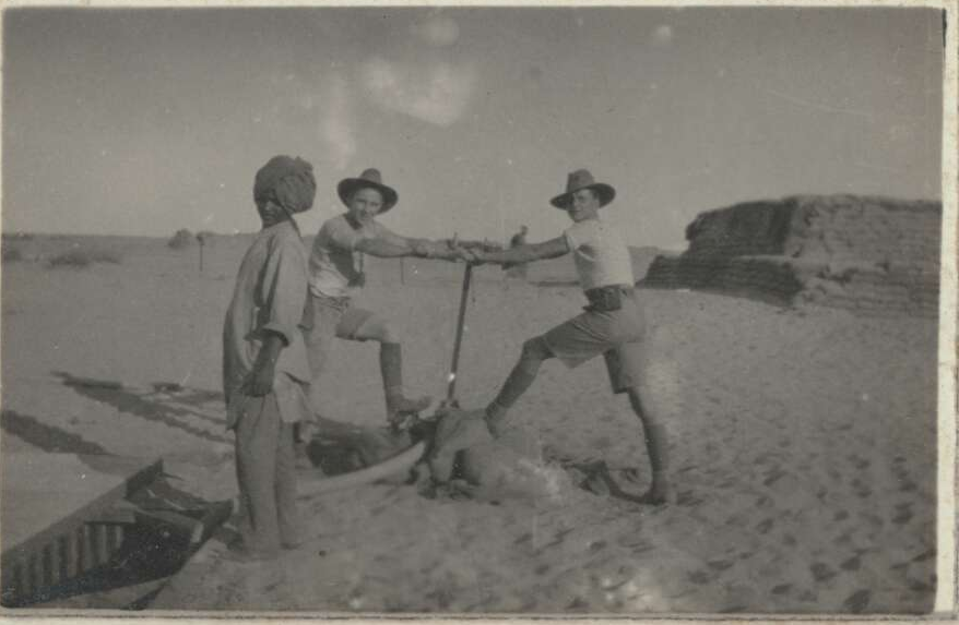 wo soldiers pumping water from a well, with a large sand-bagged emplacement in the background, Middle East