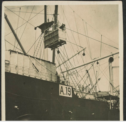 'Looking across wharf towards troop ship with crate holding a horse suspended over wharf, the number A19 on side of ship, Australian soldiers near wagon looking up at horse, an Australian soldier in left foreground.'