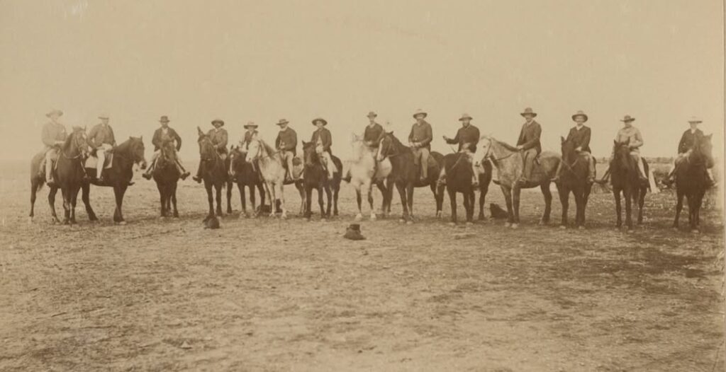'View of station hands mounted on horses, at mustering and lamb marking, Mutooroo Station. Left to right: Jimmy McKenzie, Bill Somerville, Owen Maily, Charles Ryles, [unknown], Old Ned, [unknown], Jack McKenzie, Tom Huran, Jack Rowe, Andy Huran, Tommy Horfe, [unknown], [unknown]. 1898.' Photo by Keith Mcpherson Smith State Library S.A.