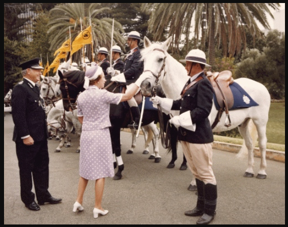 'Queen Elizabeth II patting a police horse while inspecting a row of mounted police in Perth, Western Australia, accompanied by the Police Commissioner of Western Australia Owen Leitch. Taken during the Queen's 1977 official visit to Australia. Comments: Queen Elizabeth visited Australia as part of her Silver Jubilee tour of the Commonwealth. While in Australia, she presided over the State Opening of Parliament in Canberra, visited all capital cities plus Launceston, Newcastle and other regional centres. Inscription: In an album labelled "Visit to Australia of Her Majesty The Queen and His Royal Highness The Duke of Edinburgh, 7 March to 30 March 1977".' Uni of Melbourne.